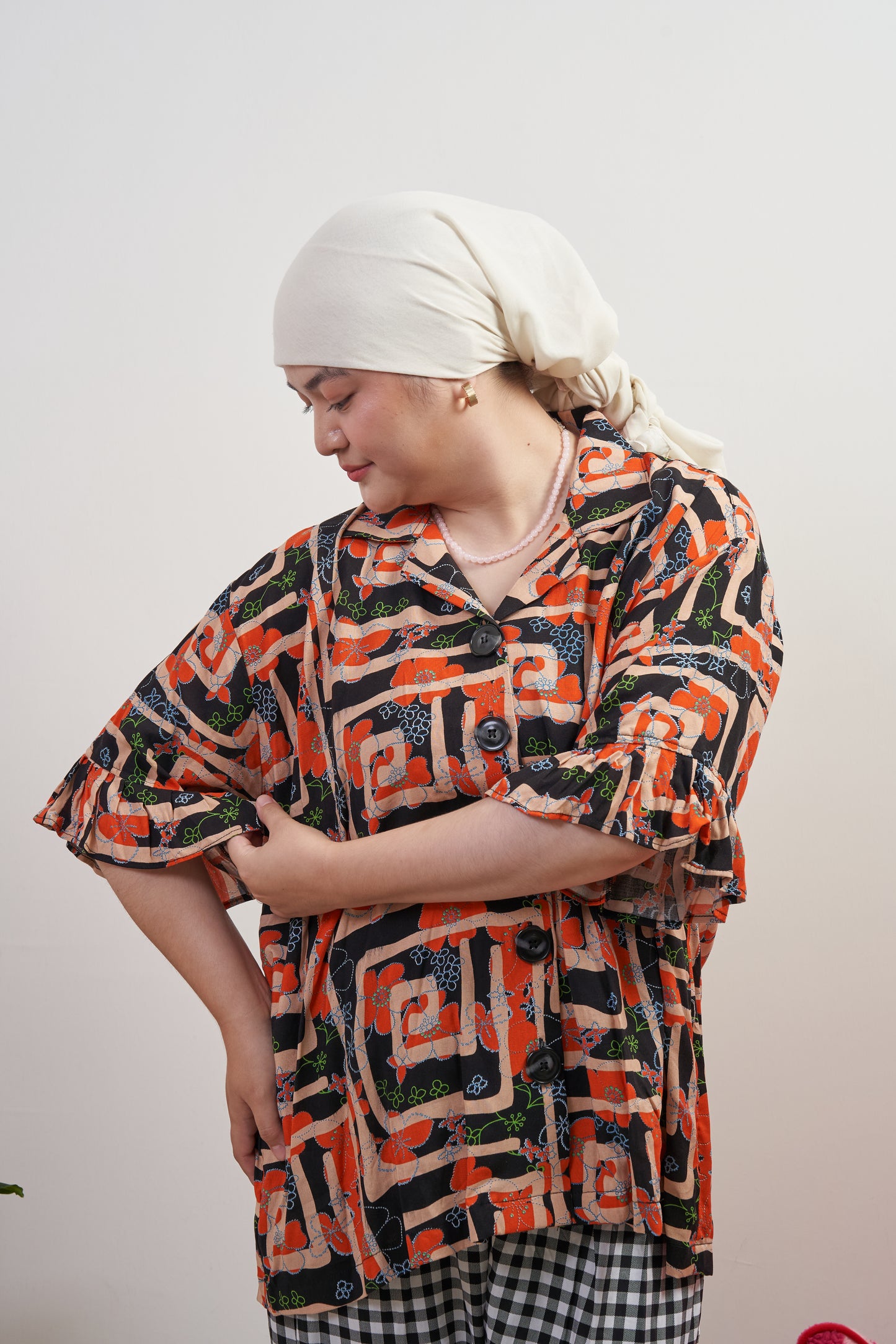 Semi-full frontal view of Buttoned Belle Blouse in Abstract Garden, model looking at ruffle detail on right sleeve, with abstract print and vintage buttons