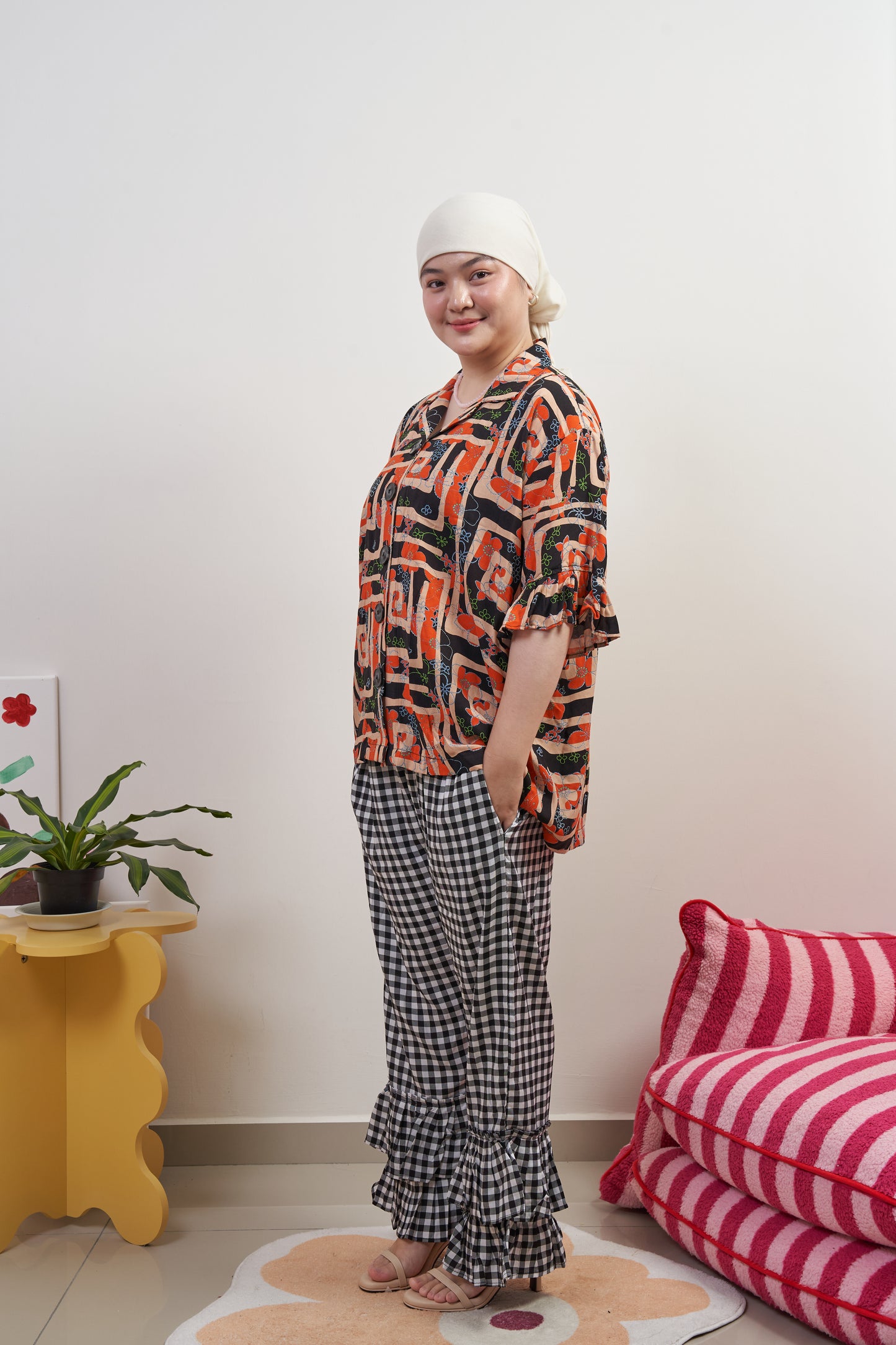 Full-body side-front profile of Buttoned Belle Blouse in Abstract Garden, model tilting body forward, paired with Flutter Flair Pants in Noir Blanc, featuring abstract print and ruffled sleeves.